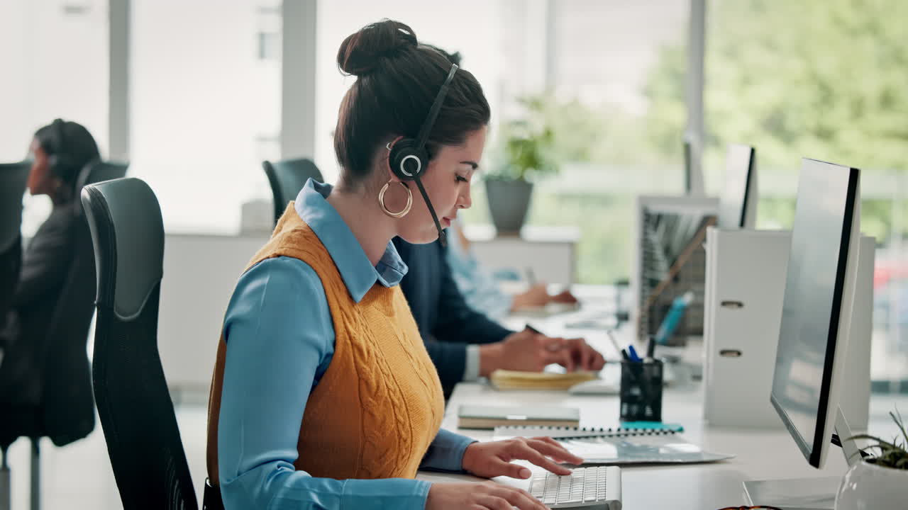 Ung kvinne med hodesett som jobber på datamaskin på et moderne kontor