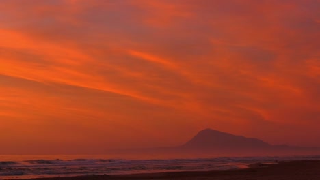 dramatic coastal seascape of orange dawn skies over sandy beach and mountain, zoom