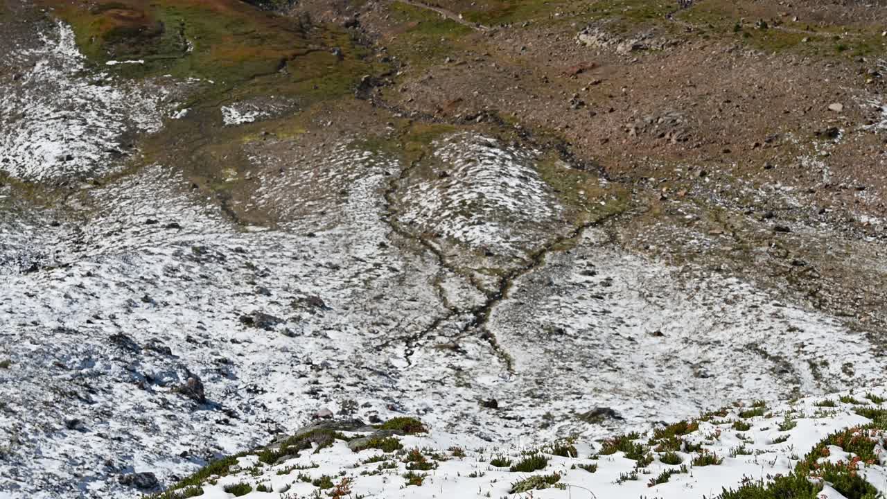 Drone shot of cracked alpine terrain with patchy snow cover and high-elevation textures in Mount Rainier National Park