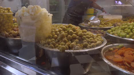 variety of olives in bowls at market with salesperson pointing, slow motion