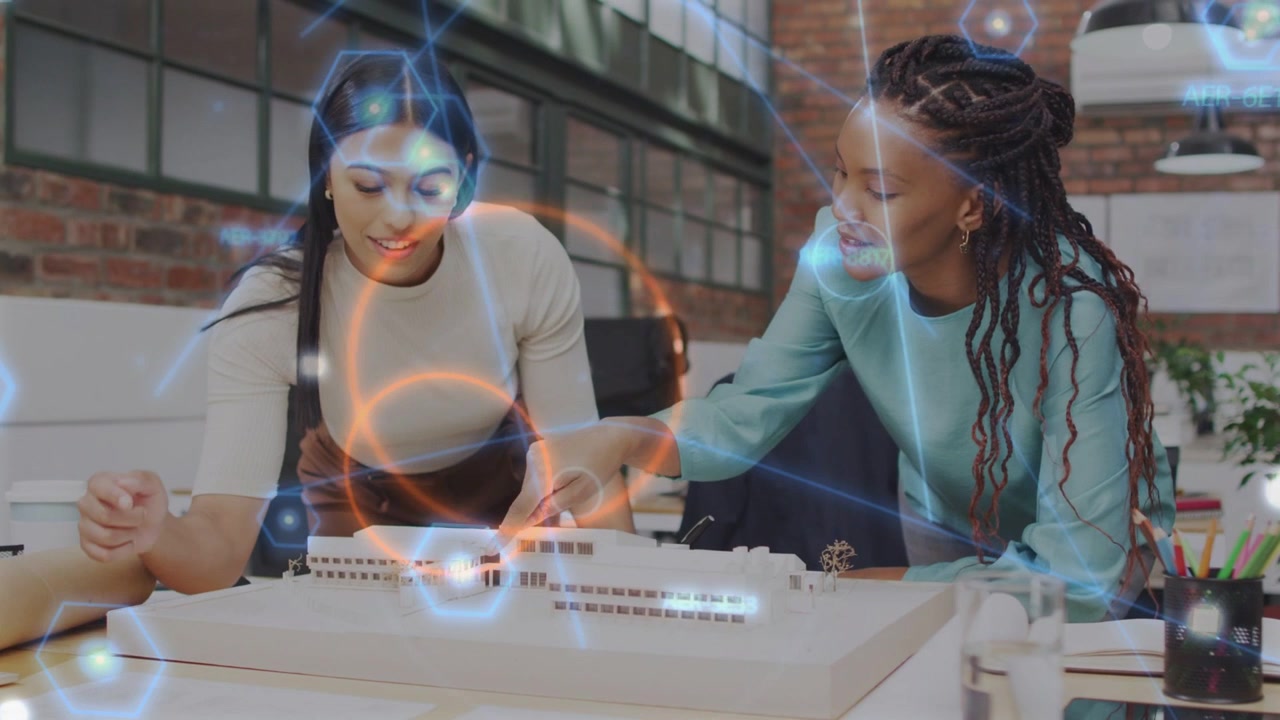 Two women leaning over design model pointing causing overlay, adjusting model for review, nodding