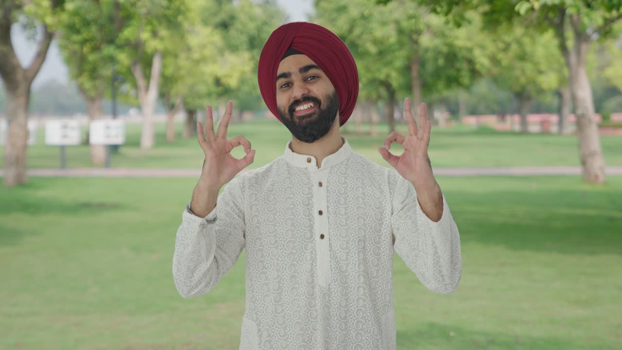 Uomo indiano Sikh felice che mostra il segno dell'okay nel parco.