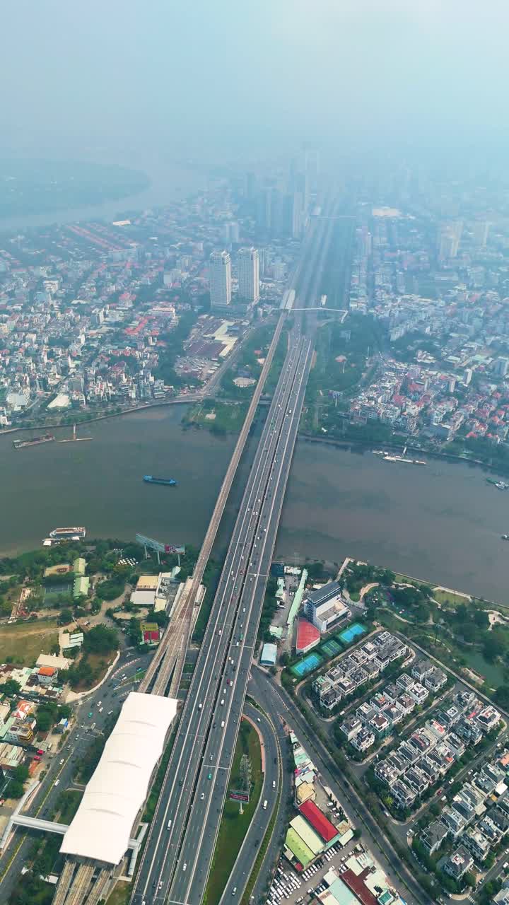 Vertical aerial: Saigon Bridge during the day with fog, traffic, cityscape, and the Saigon River in Ho Chi Minh City, Vietnam.
