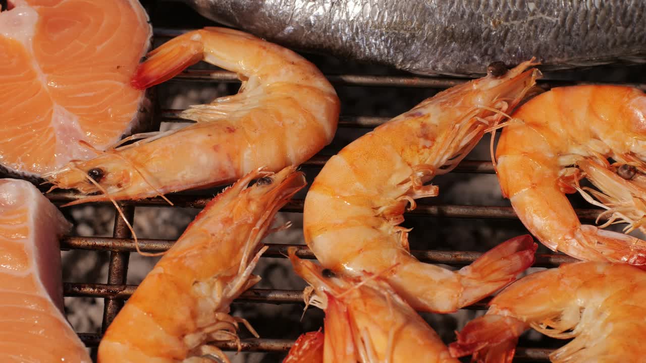 Chef cooking red salmon fish steaks with oil and spices on grill close-up. Prawns on fire throwing them on pan. Making Dorado fishes on frying grill. Restaurant Food concept. Sea food barbecue.