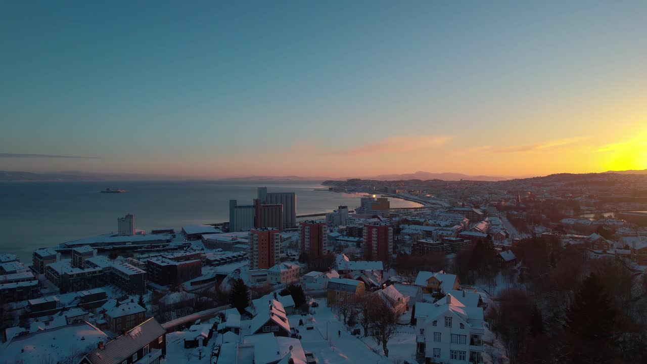 Droneopptak av Trondheim, Norge, oversiktsbilde fra luften mens solen går ned bak fjellene over byen, snødekt vinterlandskap.