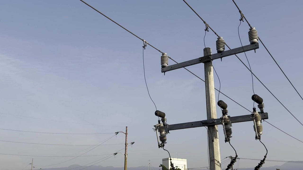 A close-up of an electric utility pole with power lines and insulators against a clear blue sky, showcasing infrastructure for electricity distribution.