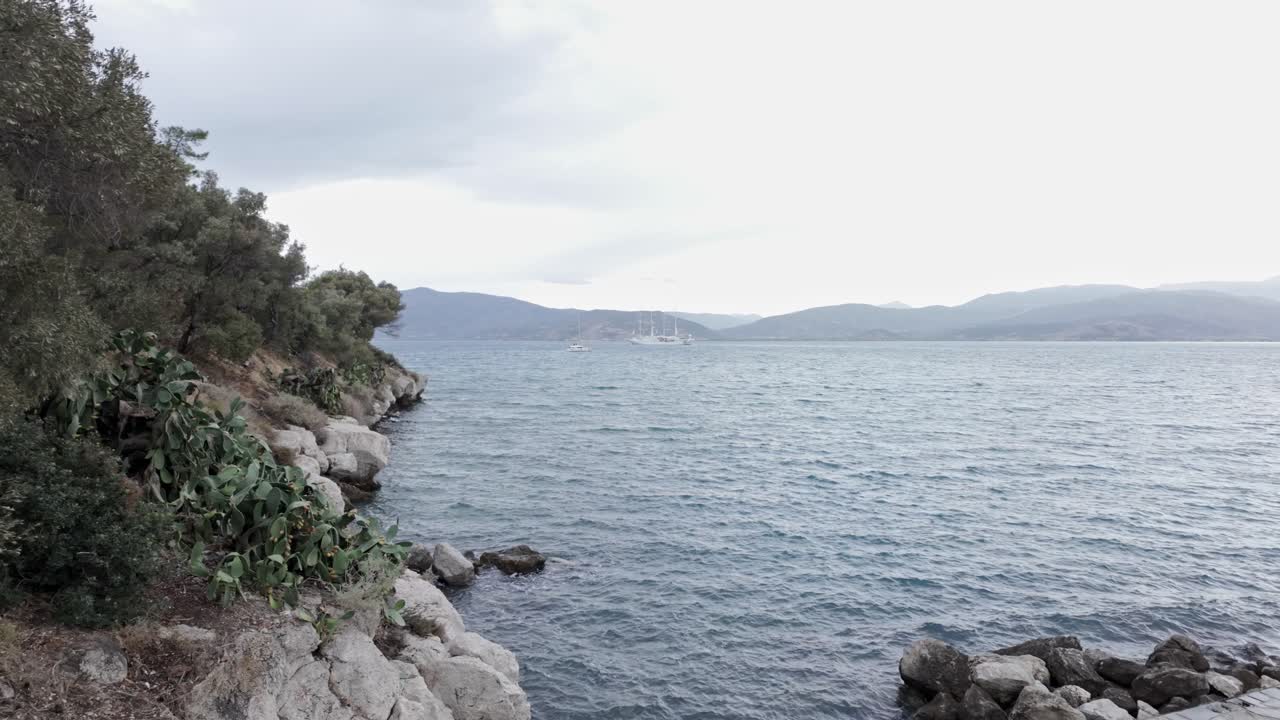 Distant ship sails off deserted rugged island coastline rainy cloudy day