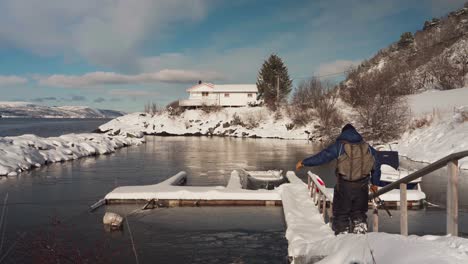 man holding fishing road walking to snowy path to jetty during winter