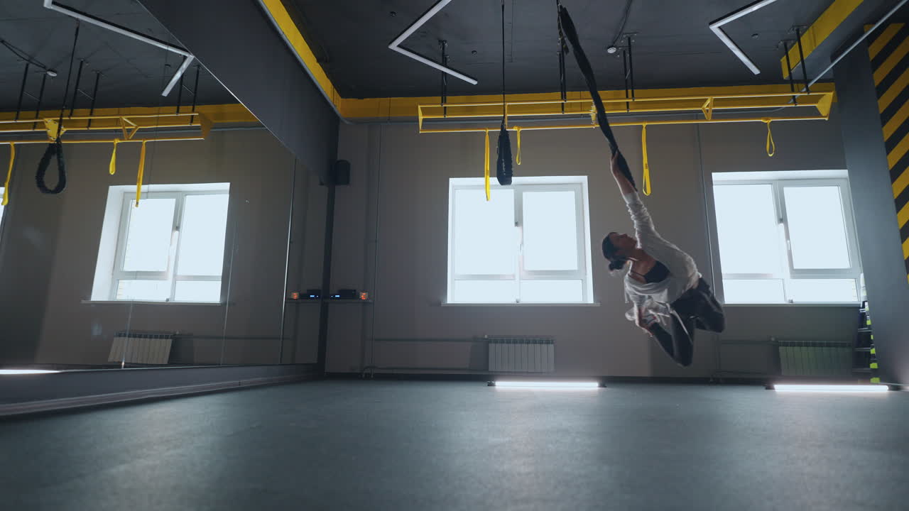 entrenamiento de estiramiento en un gimnasio moderno con sistema trx joven dama deportiva está volando sobre el piso