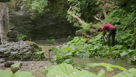 hojas verdes en el suelo mientras el fotógrafo organiza su trípode y cámara