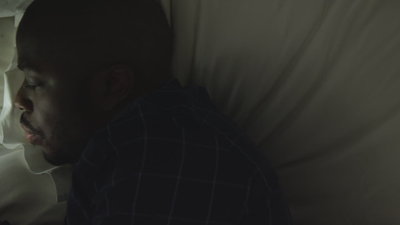 Middle Aged Man Laying On His Side In Bed Whilst Looking His Phone