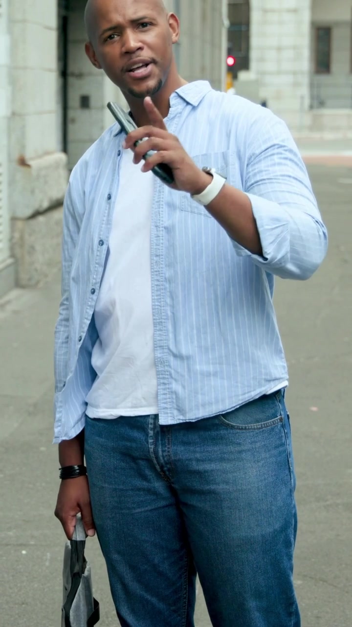 Video verticale: Un uomo in camicia blu che vede un passante, alza il telefono, saluta sul marciapiede e tiene in mano una scatola.