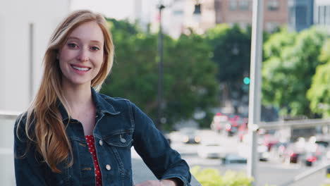 portrait of smiling young businesswoman standing outside office building with city skyline behind