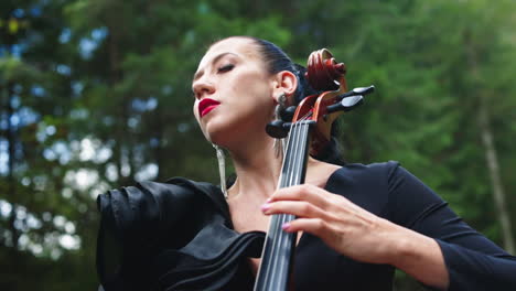 Passionate woman performs music. Attractive woman is playing the cello and enjoys the music by closing her eyes outdoors. Close-up.