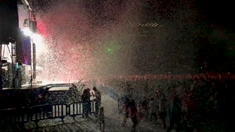 slow motion of a light and music show at a concert in a stadium with confetti shot our of canons over the audience