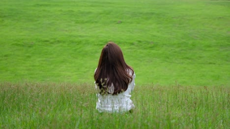 a young woman sitting on a greenery field and looking around with feeling relaxed