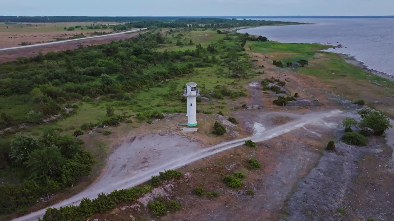 Small soviet era lighthouse on the coast with some roads and an alvar in the background