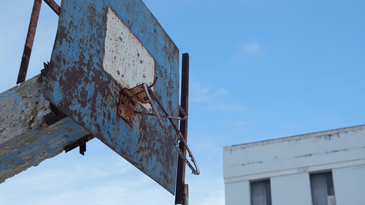 aro de baloncesto oxidado roto en un patio de recreo vacío en un cubo contra el cielo azul