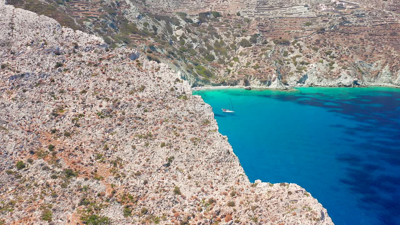 바위 절벽을 통한 공중 비행은 보트가 정박한 깨끗한 청록색 보리나 해변을 드러냅니다.