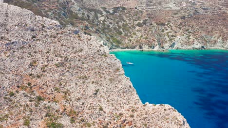 un vol aérien à travers une falaise rocheuse révèle une plage de vorina turquoise immaculée, un bateau ancré