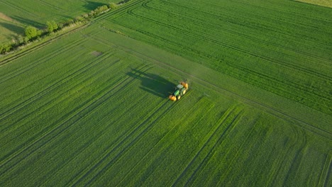 Vista-Aérea-De-Establecimiento-De-Un-Agricultor-Rociando-Campos-De-Cultivo-Con-Tractor,-Rociando-Pesticidas-Y-Fertilizantes,-Tarde-Soleada-De-Verano,-Luz-De-La-Hora-Dorada,-Tiro-Amplio-De-Drones-De-Ojo-De-Pájaro