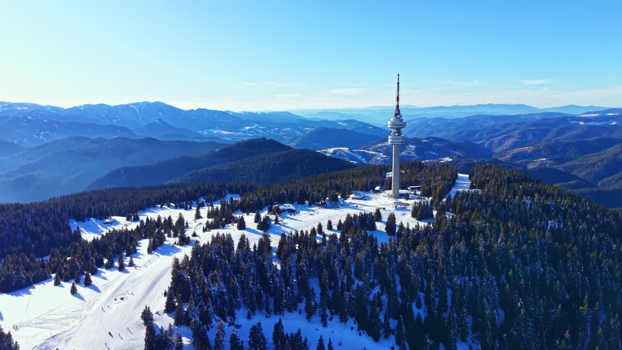 Letecký pohled na komunikační věž na zasněženém horském vrcholu s borovicovým lesem