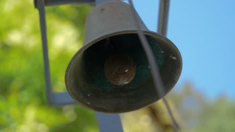 close up on a small black cast iron bell with trees in background in slowmotion in france