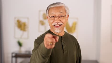 an elderly asian man with gray hair and glasses points and smiles at the camera in a bright, modern indoor setting with soft lighting