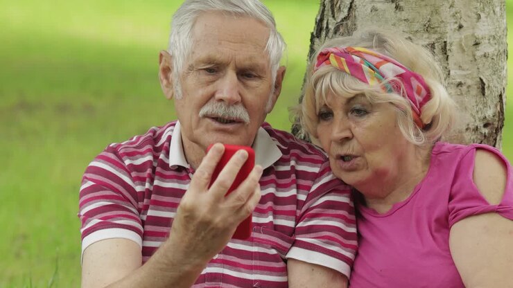 Picnic in famiglia. Coppia di anziani nonni al parco che usano lo smartphone per navigare online e fare acquisti.