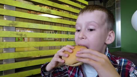 school boy eating hamburger. happy child eating fast food in restaurant