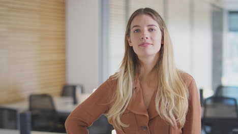 Portrait-Of-Smiling-Businesswoman-Walking-Into-Focus-In-Modern-Open-Plan-Office