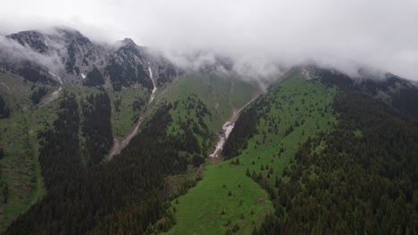 Toma-Aérea-De-Las-Montañas-Piatra-Craiului-Bañadas-Por-Nubes-Con-Exuberantes-Laderas-Verdes