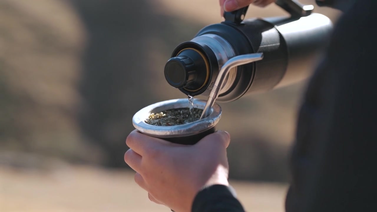 Hot water poured into a yerba mate gourd outdoors in Argentina, featuring traditional preparation, social customs and South American beverage culture, close-up shot.