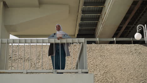 Black-Muslim-woman-rests-leaning-on-railing-under-bridge