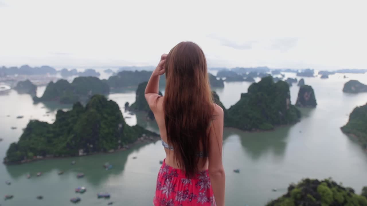 Experience serenity as a woman stands alone on a picturesque island, basking in the breathtaking view of endless blue waters and lush greenery