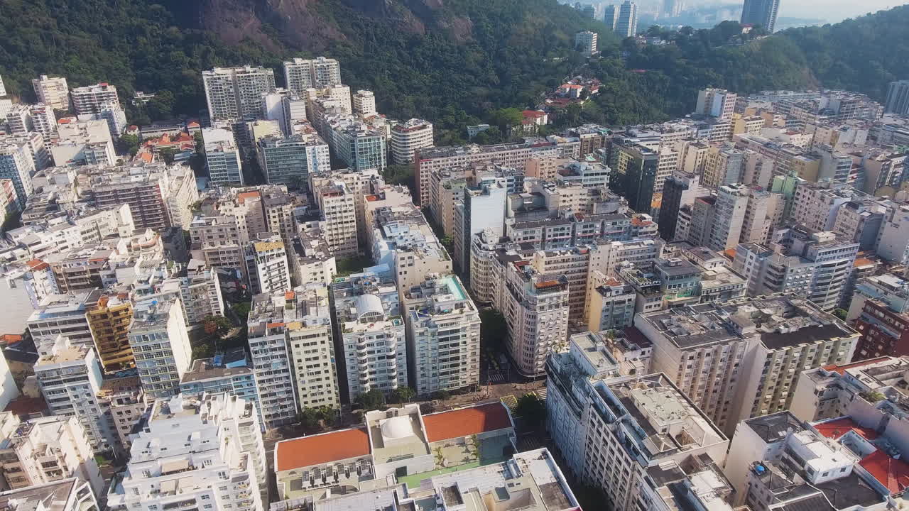 Drone avança sobre telhados do Rio com morros florestados ao fundo