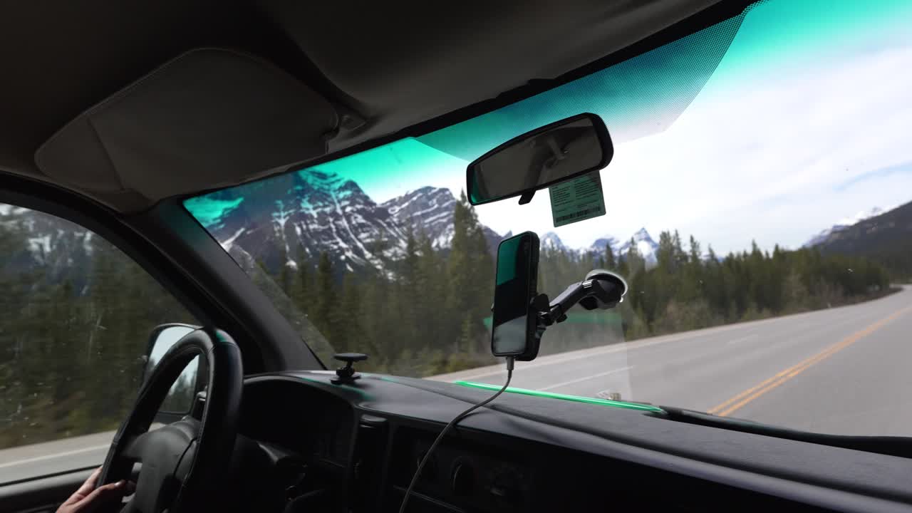 Uomo alla guida di un camper in viaggio su strada, che attraversa montagne e foreste delle Montagne Rocciose canadesi