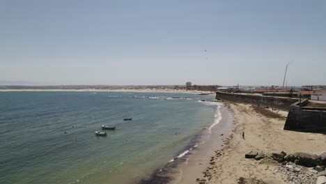 Waves-crashing-on-long-sand-beach-with-walled-fortress,-Peniche,-Portugal