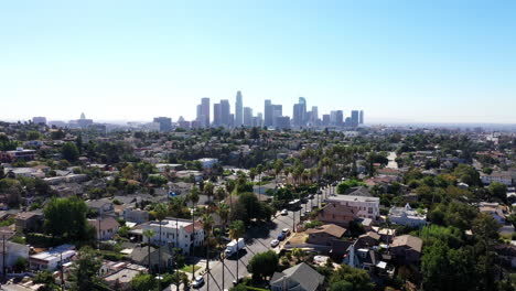 beautiful drone shot of los angeles, california showing neighborhoods, streets, cars, mansions, palm trees and the city skyline against a blue sky during golden hour