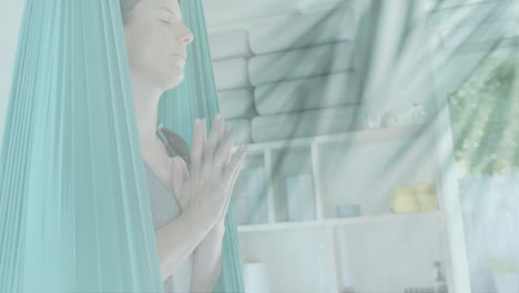 Animación-De-Hojas-De-Plantas-Sobre-Una-Mujer-Caucásica-Feliz-Meditando-En-Una-Clase-De-Yoga-Aéreo