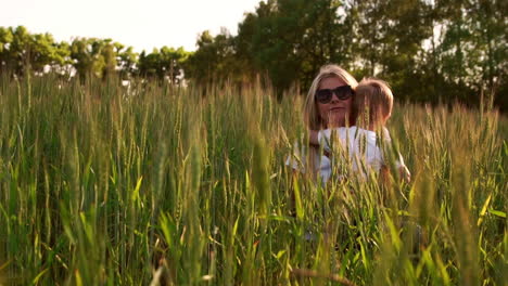 Loving-mom-and-son-hugging-and-playing-with-a-soccer-ball-in-a-field-with-spikelets-in-beautiful-sunset-light-in-white-t-shirts