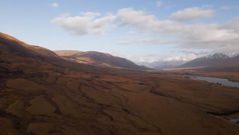 Golden-brown-hillside-with-snow-capped-mountains-and-a-lake-in-background