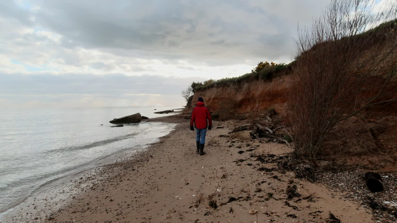 Un uomo cammina lungo la baia della spiaggia al tramonto sotto un cielo nuvoloso vicino a una scogliera