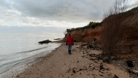 man walking along the beach bay at sunset under a cloudy sky near a cliff