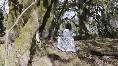 shaman woman kneeling at the base of a maple tree and thanking her ancestors