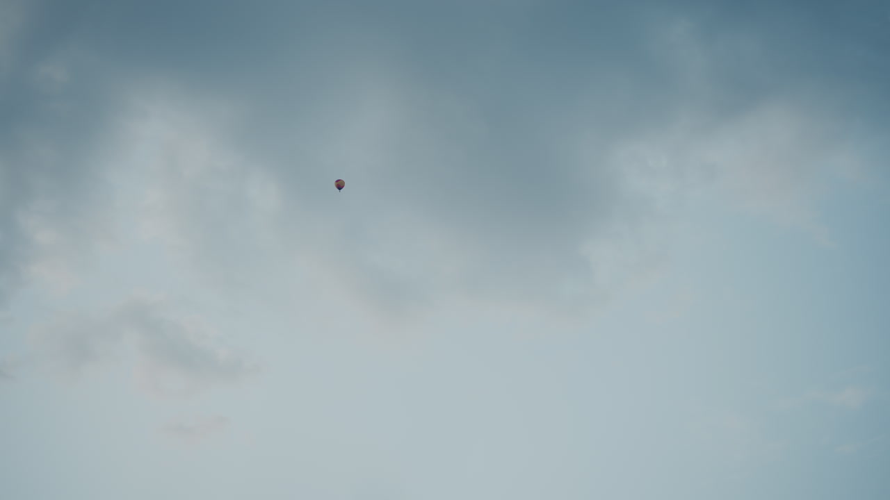 passenger in hot air balloon flying above vast open fields under dramatic cloudy sky at dawn soft light casting gentle hues across distant horizon capturing peaceful aerial journey vibe