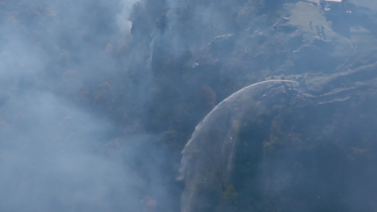imágenes aéreas en cámara lenta de un grupo de bomberos en un acantilado rociando agua en un incendio forestal en lookout mountain.