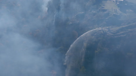imágenes aéreas en cámara lenta de un grupo de bomberos en un acantilado rociando agua en un incendio forestal en lookout mountain.