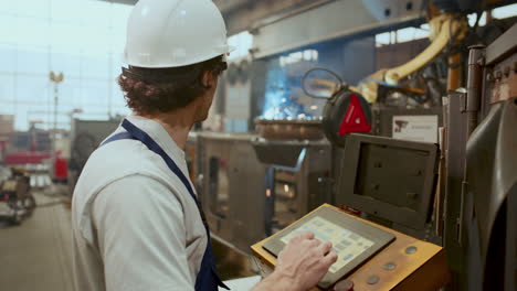 factory worker operating welding machine with control panel