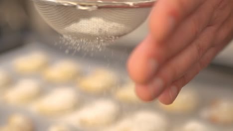 a baker sifting powdered sugar on freshly baked vanilakipferl cookies